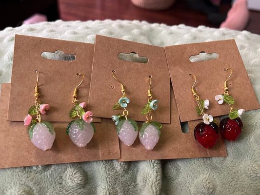 Two pairs of earrings on brown card holders against a textured surface.